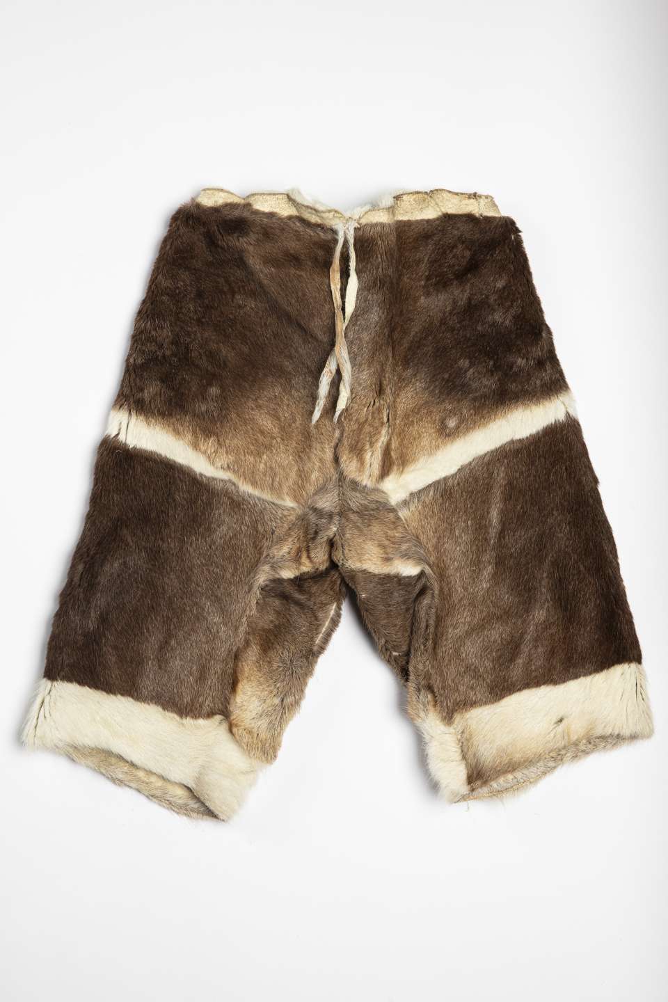 Pantalon en fourrure brune, vu de derri&egrave;re, avec une bande lat&eacute;rale de fourrure blanche au milieu et une au bas de chaque jambe. Un cordon en cuir retourn&eacute; pend &agrave; la taille.