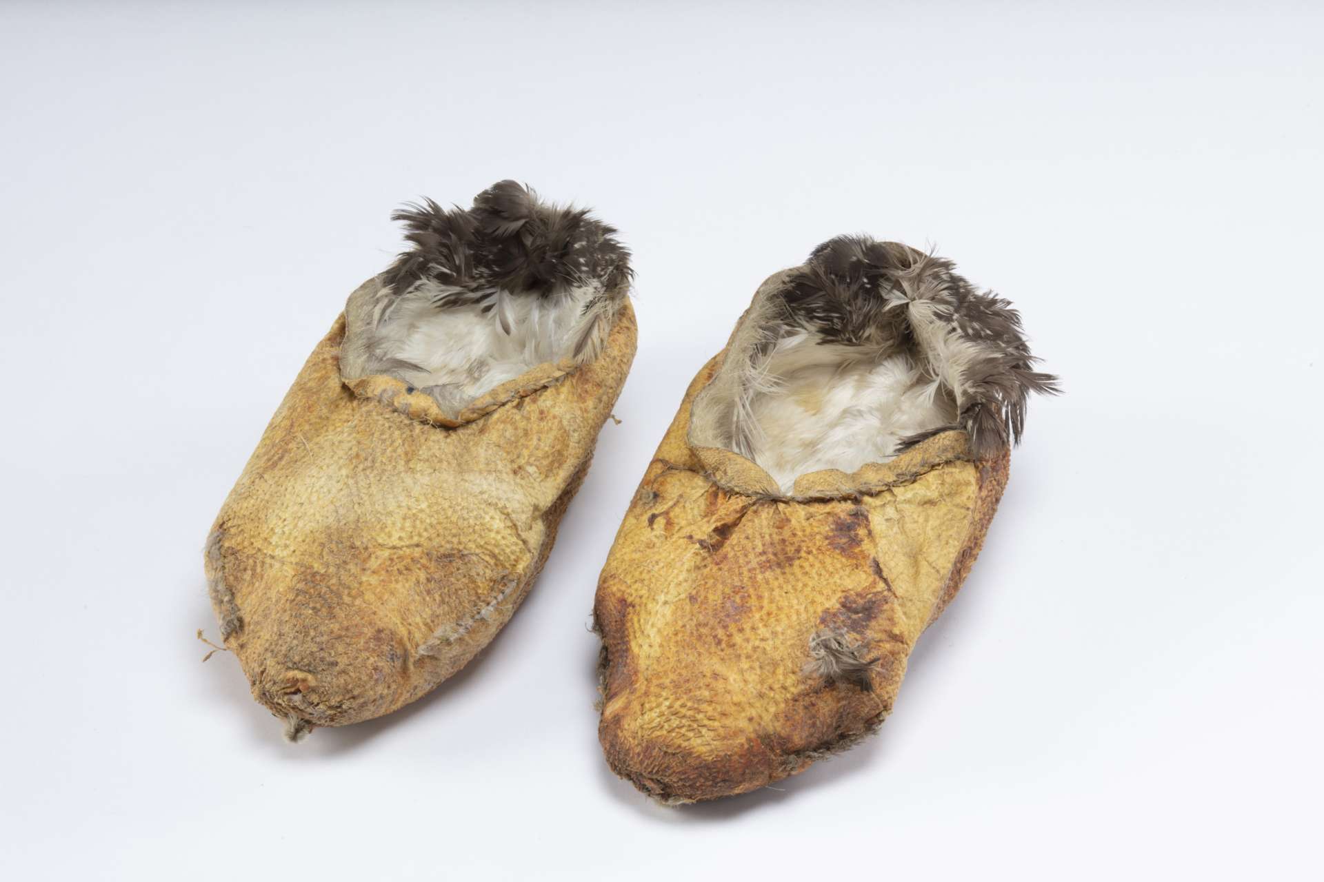 Deux chaussons en peau de huard retourn&eacute;e, de couleur brun orang&eacute;, avec des plumes p&acirc;les et fonc&eacute;es visibles &agrave; l&rsquo;int&eacute;rieur.