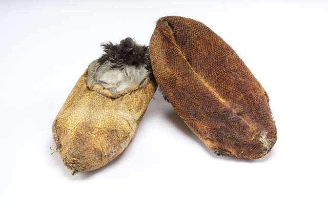 Deux chaussons en peau de huard retourn&eacute;e, de couleur brun orang&eacute;, avec des plumes p&acirc;les et fonc&eacute;es &agrave; l&rsquo;int&eacute;rieur. L&rsquo;un des chaussons est tourn&eacute; pour montrer la semelle textur&eacute;e et la couture transversale.