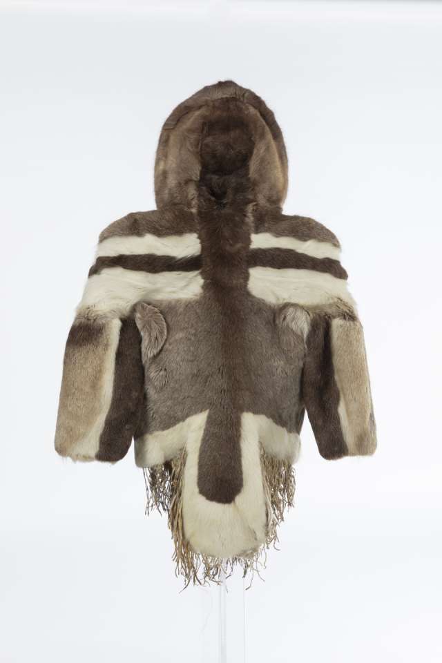 Manteau en fourrure, vu de derri&egrave;re, au capuchon relev&eacute; montrant les bandes de fourrure horizontales claires et fonc&eacute;es sur les &eacute;paules et le dos. Le pan arri&egrave;re du manteau, bord&eacute; de blanc, se termine par une pointe arrondie, prolong&eacute;e de franges.