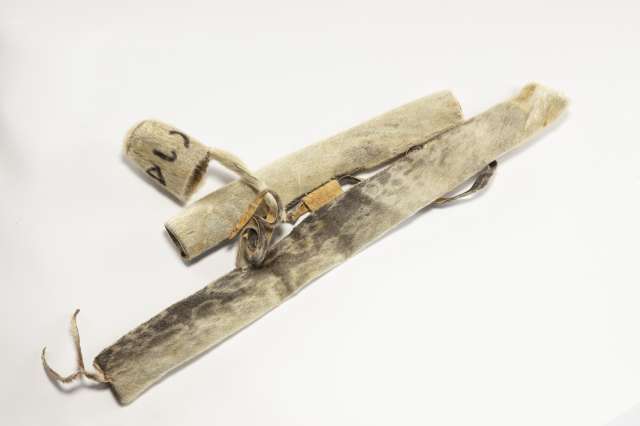 Deux &eacute;tuis cylindriques dispos&eacute;s l&rsquo;un &agrave; c&ocirc;t&eacute; de l&rsquo;autre. Le premier est en peau de phoque sombre avec des taches plus claires en forme d&rsquo;anneaux. Le second est plus court et en fourrure beige p&acirc;le, reli&eacute; &agrave; son capuchon par une lani&egrave;re enroul&eacute;e, sur lequel est &eacute;crit, en fourrure brune, &laquo; ugatu &raquo; en inuktitut syllabaire.