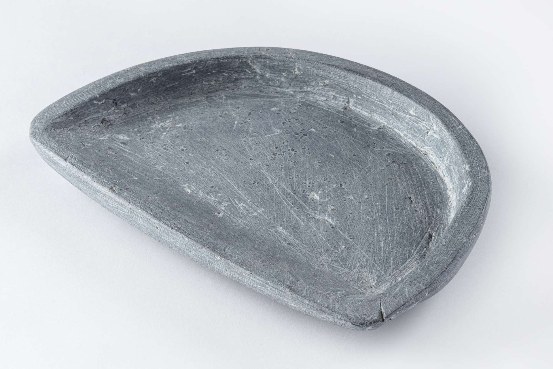 Lampe &agrave; l&rsquo;huile en roche grise et lisse de forme demi-circulaire avec un creux central. La surface de la lampe montre des &eacute;gratignures.