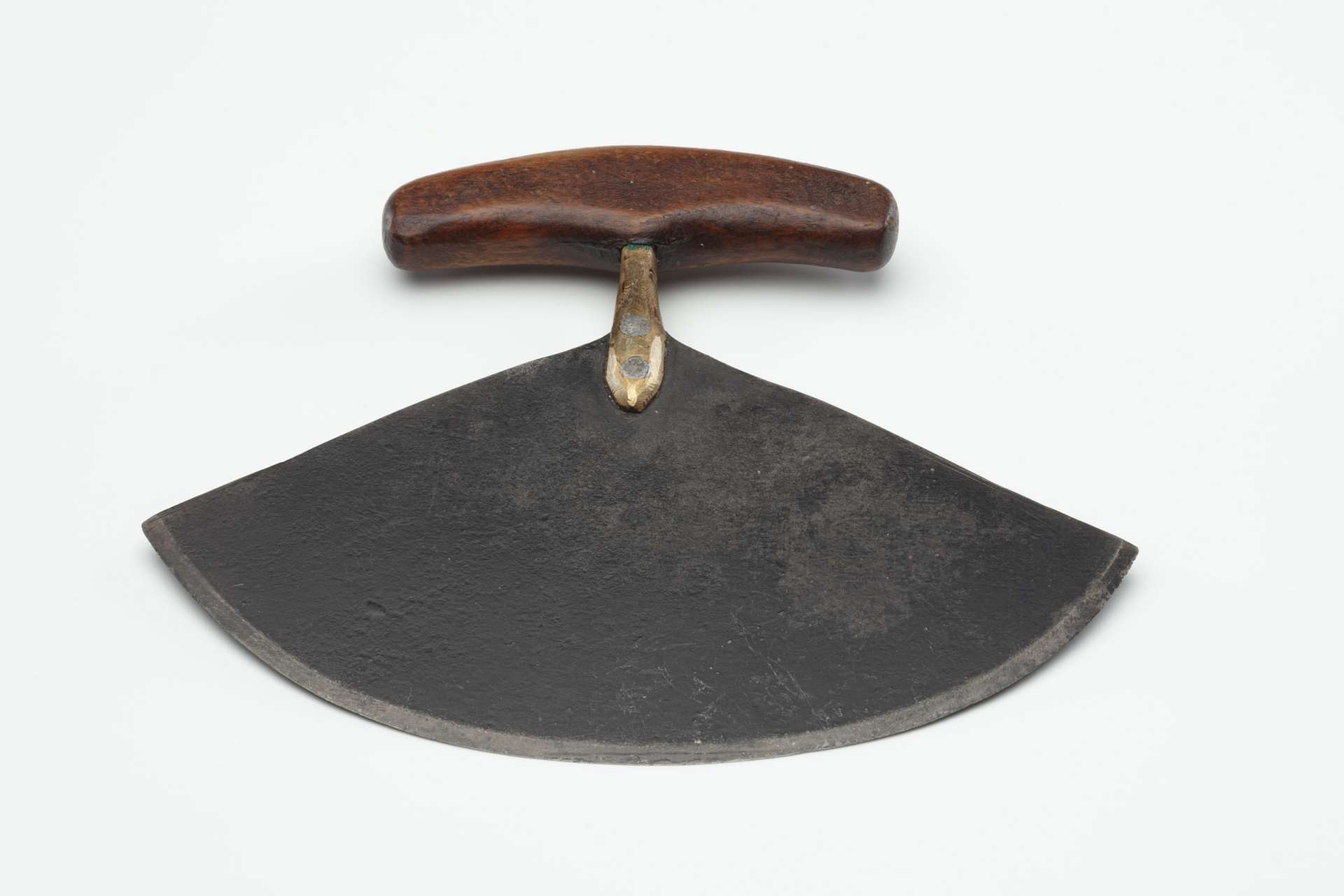 Couteau, vu de face, avec une grande lame semi-circulaire en m&eacute;tal. La lame est fix&eacute;e au manche en bois sombre par un support clout&eacute; de deux rivets m&eacute;talliques.