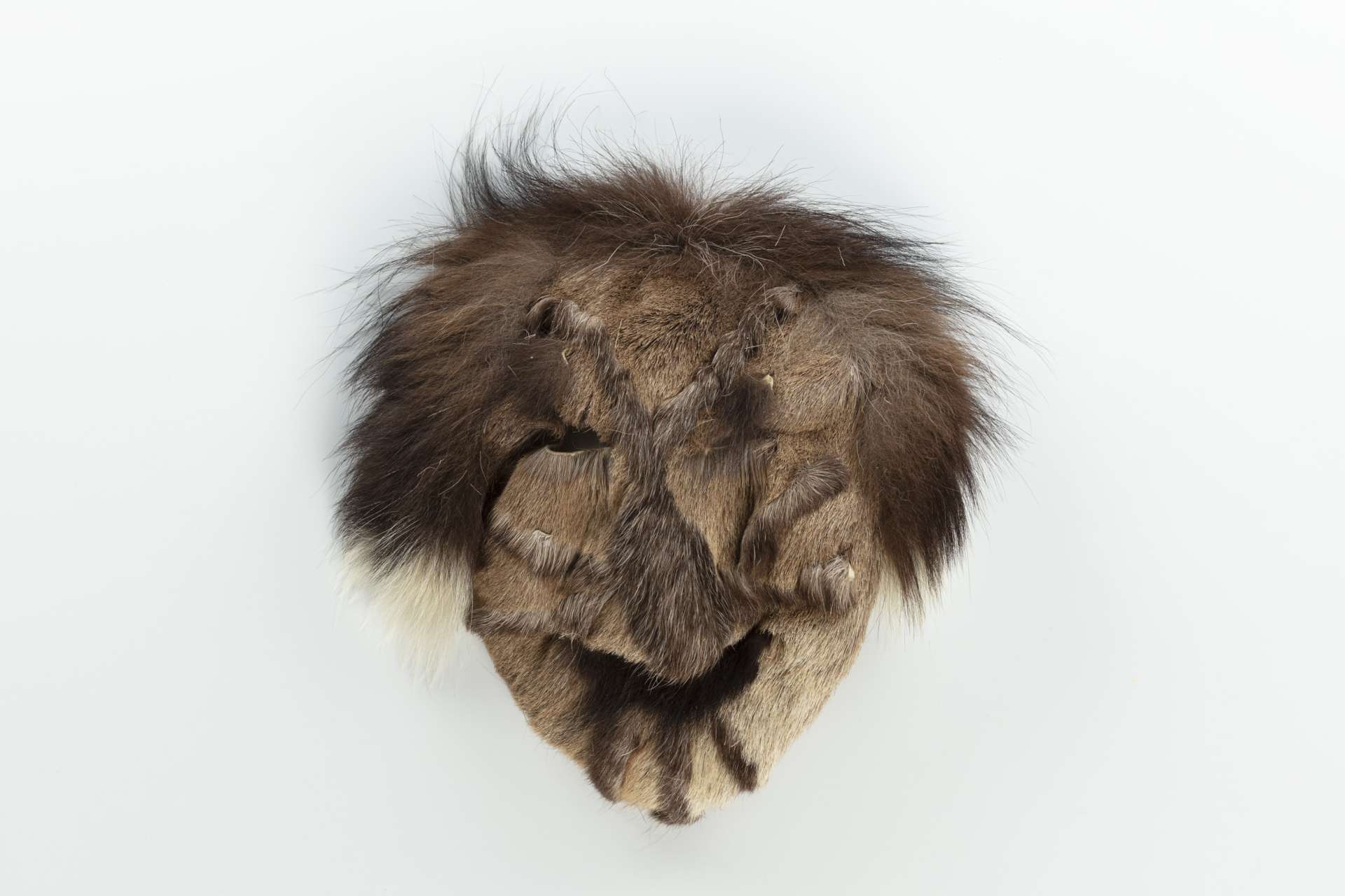 Masque en fourrure, vu de face, avec des sections brun plus fonc&eacute;, simulant des tatouages faciaux. Deux ouvertures sont apparentes au niveau des yeux et une bande de fourrure fonc&eacute;e simule un sourire.